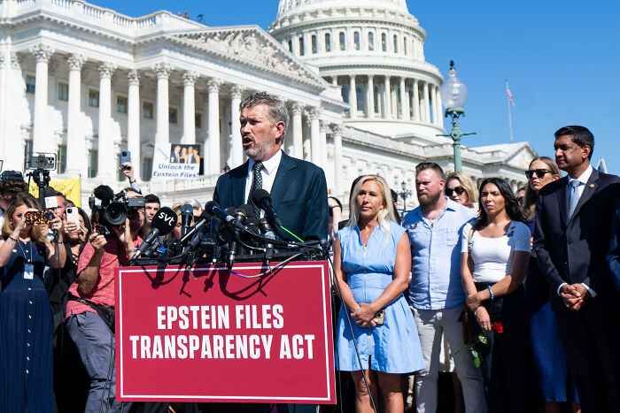 Man speaking at a podium with Epstein Files Transparency Act sign, with Lauren Boebert and others outside US Capitol building.