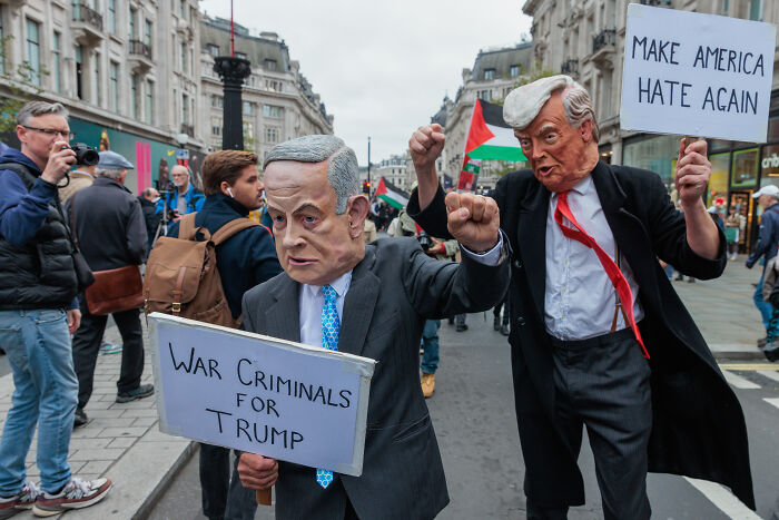 Protesters wearing political masks hold signs criticizing Trump, reflecting ex-Trump fans losing hope in 2025.