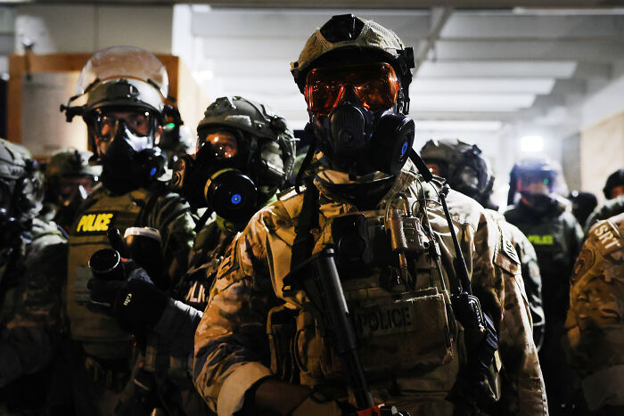 Law enforcement officers in tactical gear and gas masks preparing for ICE raids during a MAGA fan viral incident.