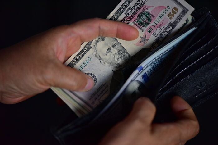 Hands holding a wallet with cash, illustrating Americans living paycheck to paycheck in a financial struggle concept.