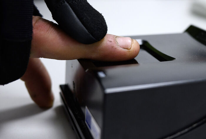 Close-up of a finger scanning on a biometric device representing migration control in surveillance states and data clouds.