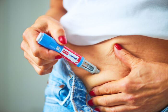 Close-up of hands with red nails using an injection pen on skin, unrelated to Donald Trump&rsquo;s face or fainting incident.