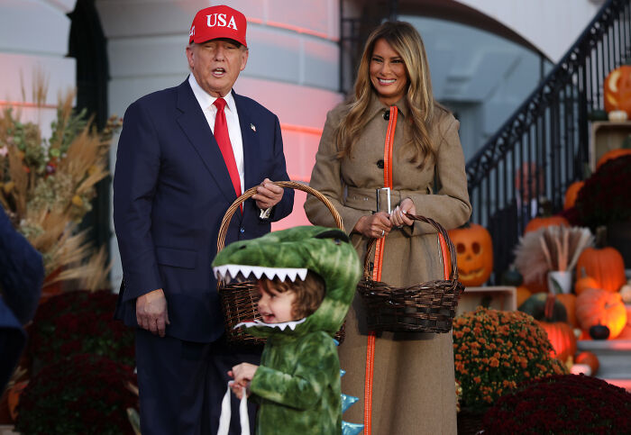 Melania Trump and Donald Trump at White House Halloween event with child in dinosaur costume, seasonal decorations in background
