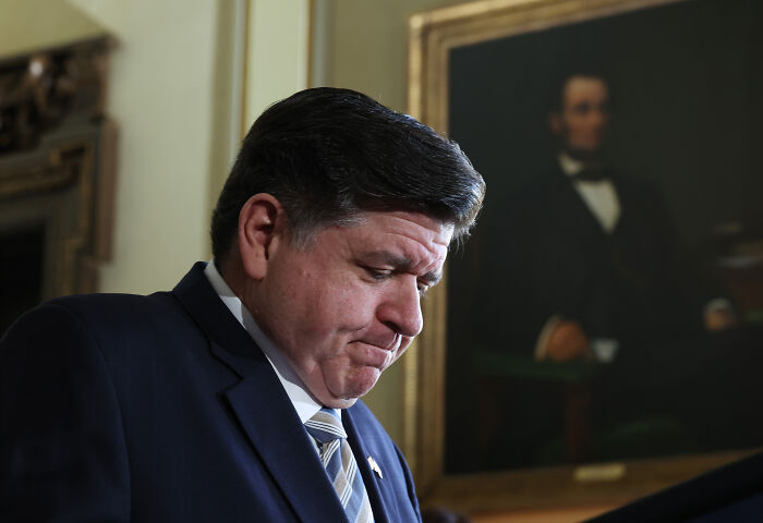 Illinois Governor J.B. Pritzker looking down solemnly during a press event in Chicago amid ICE withdrawal discussions.