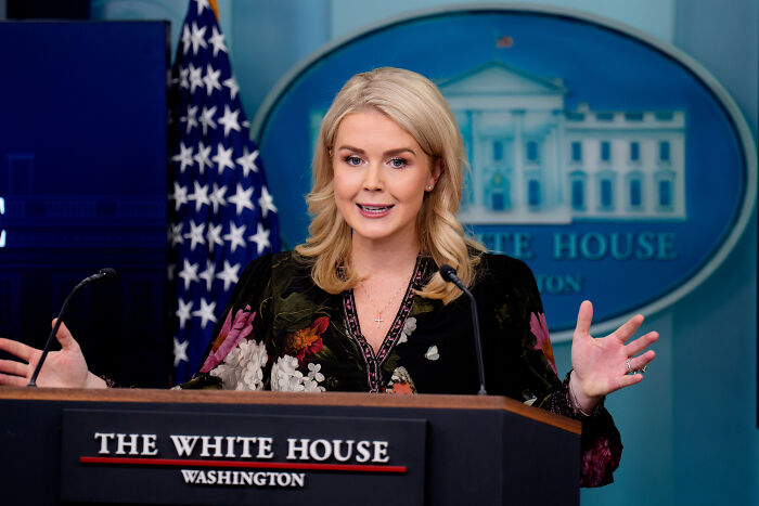 Karoline Leavitt speaking at the White House podium with American flag in the background, discussing Trump insult context