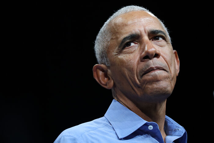 Barack Obama in a blue shirt looking pensive against a dark background related to Trump&rsquo;s all-night rage posts topic.