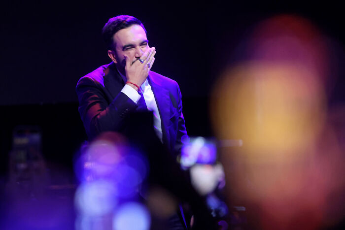 Zohran Mamdani in a dark suit delivers NYC mayoral victory speech, pledging to turn the volume up in political battle.