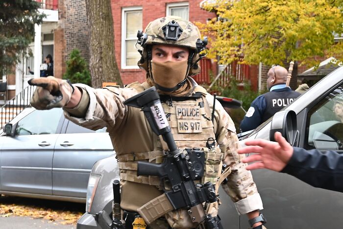 Armed ICE officer in tactical gear directing traffic during operation amid Chicago withdrawal discussions.