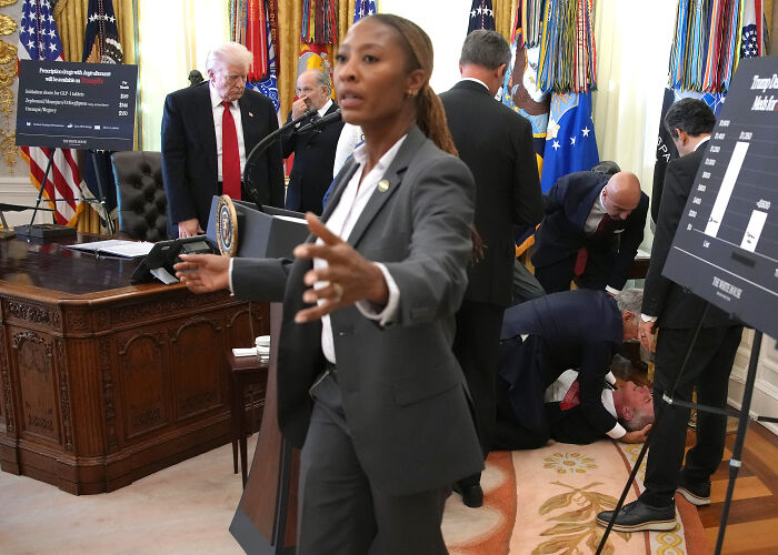 Donald Trump in Oval Office with a man fainting behind him and people attending to the situation quickly.