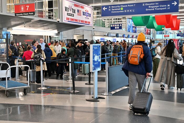 Travelers wait in long security lines at an airport amid news of Democrats caving to Trump as senators reach shutdown deal.