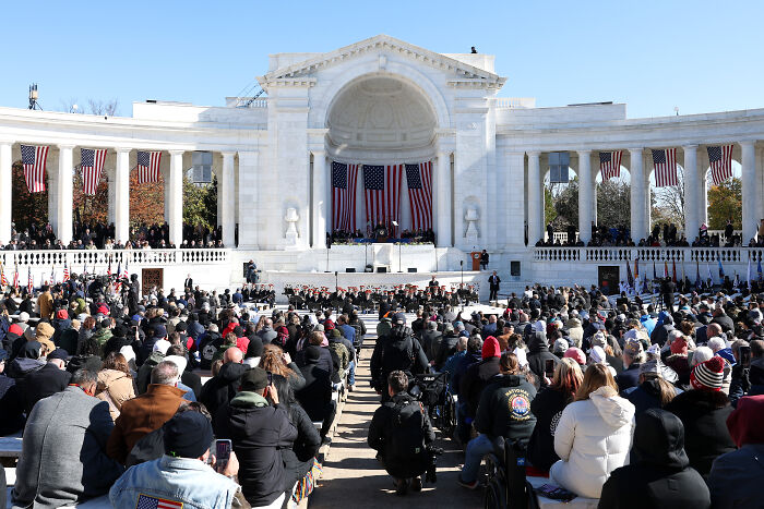 Large crowd gathered at a memorial event honoring fallen heroes with American flags, reflecting Veterans Day tribute and Russian twist.