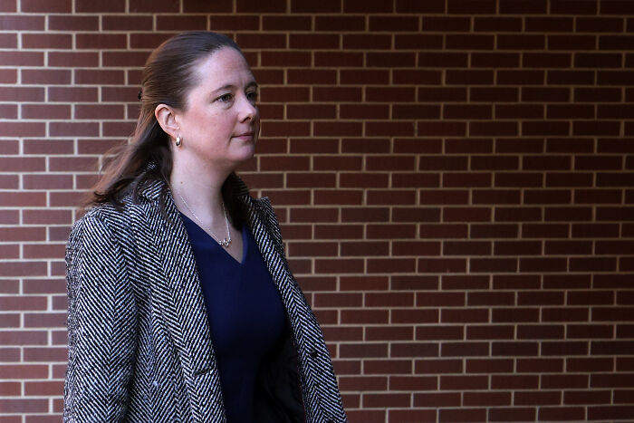 Woman in patterned coat walking past brick wall, related to Trump DOJ resignation letters in web archive revelation.