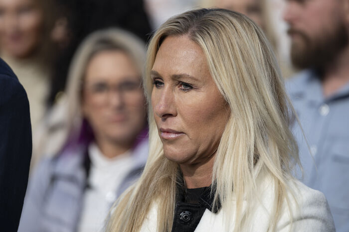 Marjorie Taylor Greene speaking seriously in a public setting, addressing GOP men amid resignation defense.