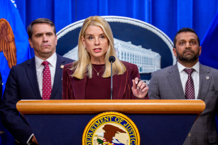 Woman speaking at a Department of Justice podium during a press conference, with FBI files mentioned in context.