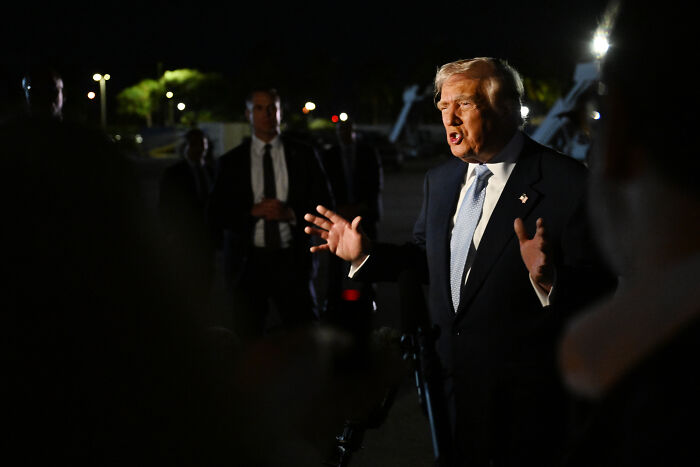 Donald Trump speaking urgently at night with security and press in the background, reacting to questions on Epstein files.