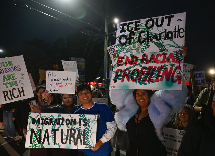 Protesters holding signs against ICE raids and advocating for migration rights during a nighttime demonstration.