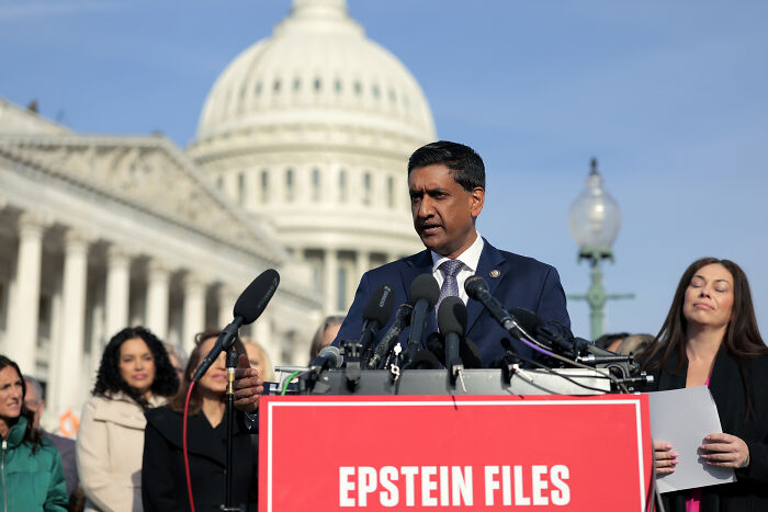 Man speaking at a podium with Epstein Files sign, several people behind him, US Capitol building in the background at a press event