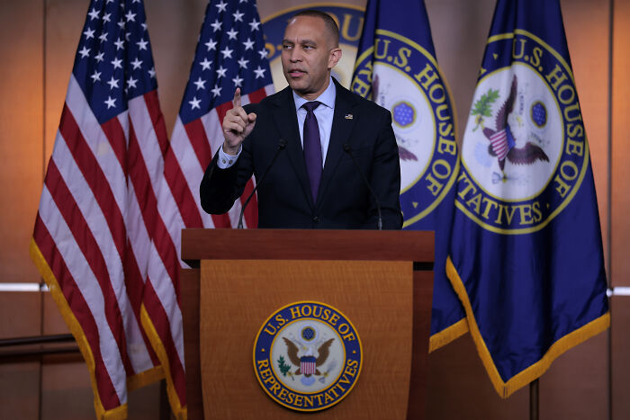 U.S. representative speaking at podium with flags warning of political violence and sedition risks.