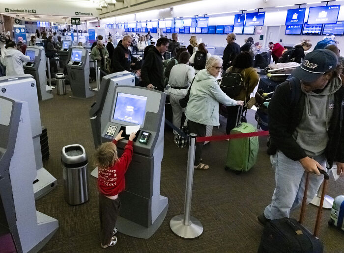 Busy airport terminal with travelers using self-check-in kiosks, highlighting Gavin Newsom's response to airport dress code advice.