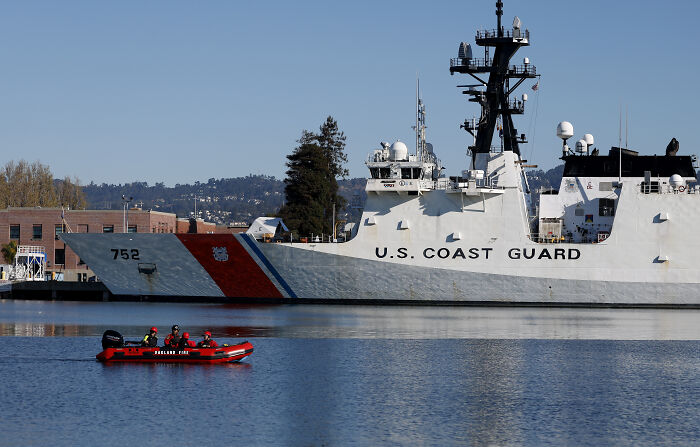 U.S. Coast Guard ship docked with a small boat nearby, highlighting Trump claims on redesigned ship aesthetics.