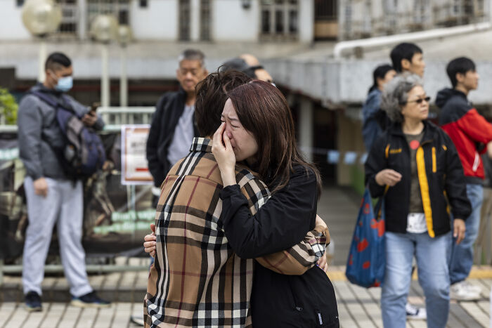 Grieving people embrace near Hong Kong apartment complex after fire with fatalities rising to 128, officials report.