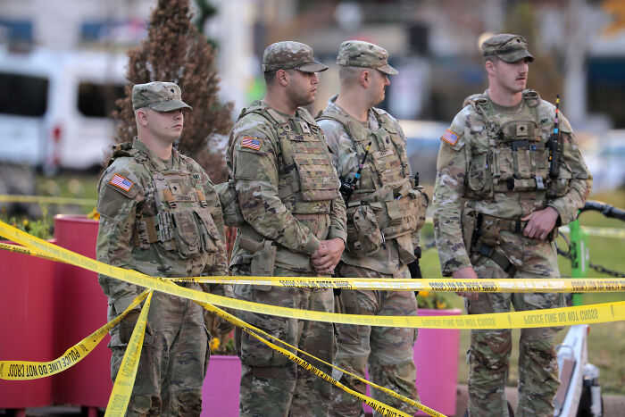 National Guard soldiers stand behind police tape at a secured crime scene related to a gunman incident.