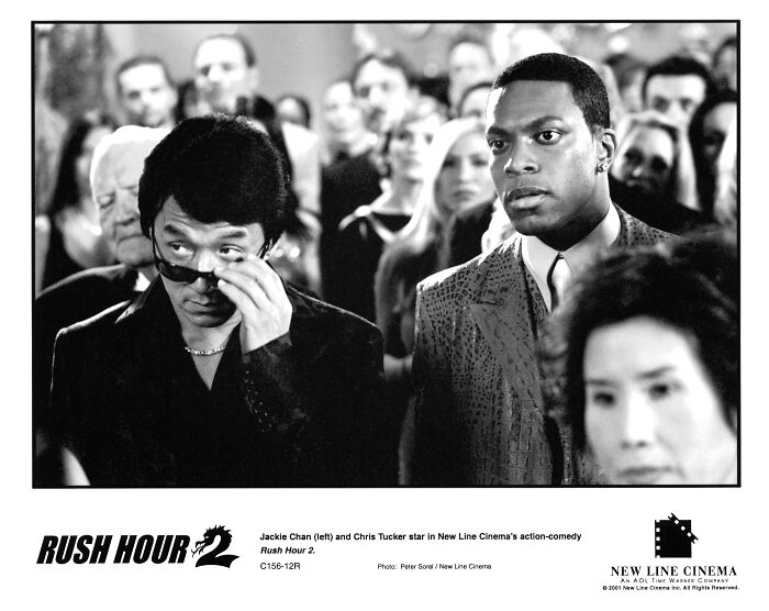 Black and white still from Rush Hour 2 featuring Jackie Chan and Chris Tucker in a crowded scene from the Hollywood movie franchise.