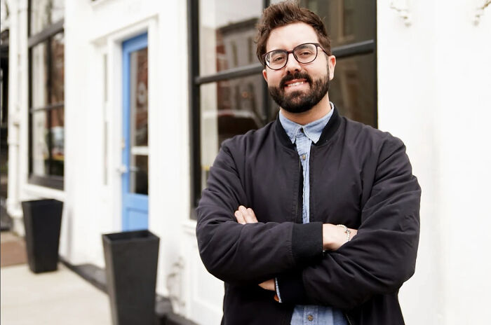 Man with glasses and beard standing confidently outside a building, relating to Vance clan setback in Cincinnati election.