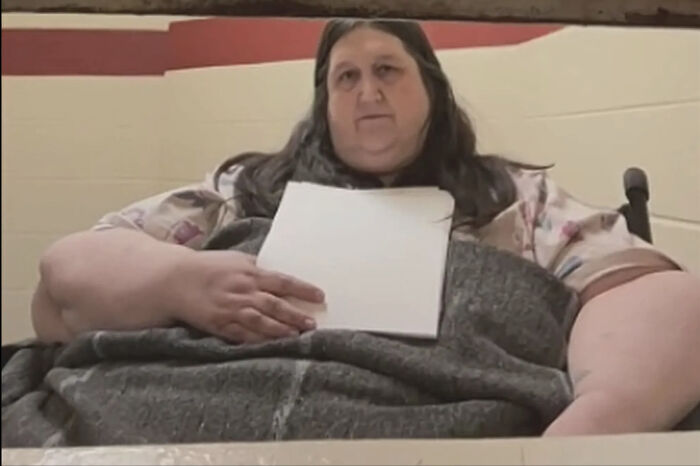 Overweight woman sitting indoors holding a piece of paper, related to neglect and starvation case of a 14-year-old girl.