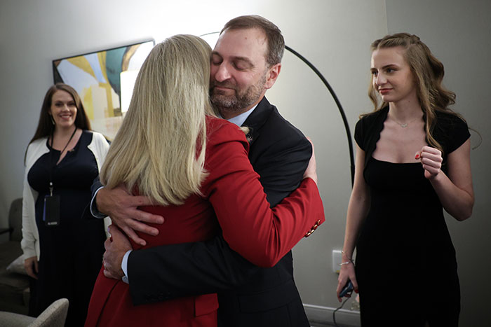 Man in suit hugging woman in red jacket as Virginia turns blue in a sweeping victory, marking a heavy blow for Trump.