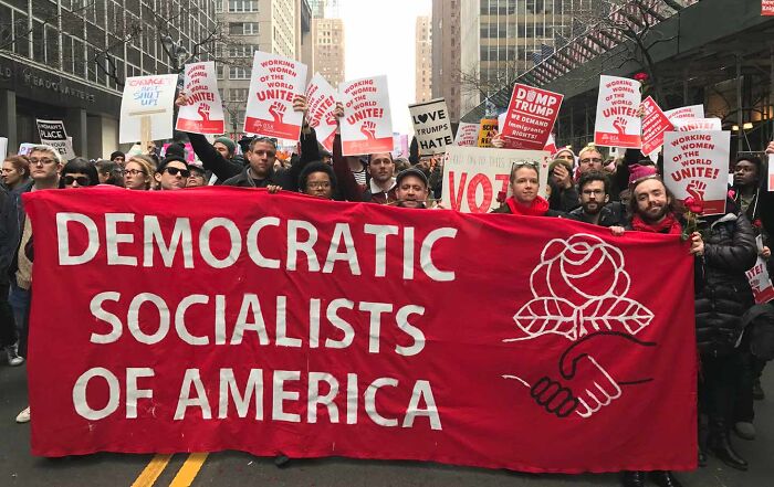 Protesters holding a red banner for Democratic Socialists of America during a rally in a city street.