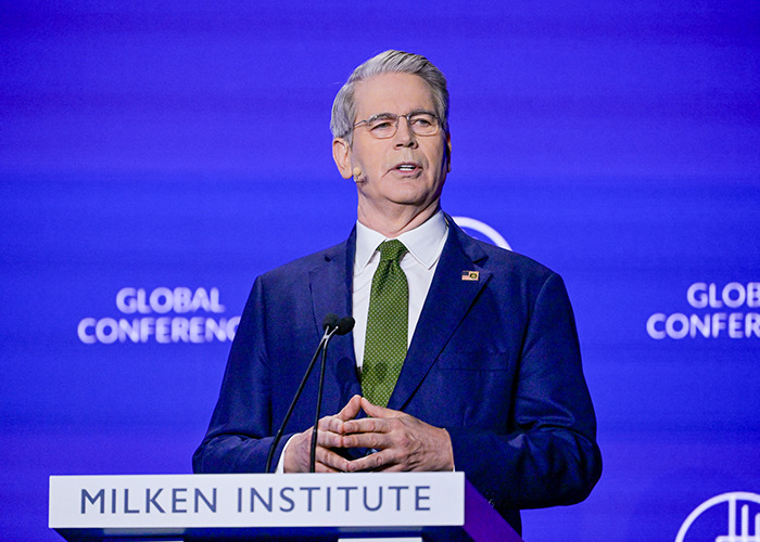 Man in suit and glasses speaking at Milken Institute event on new energy and G20 powers ahead with global conference backdrop.