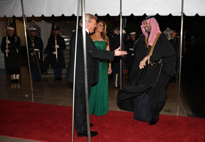 Melania Trump making a subtle gesture to Saudi Crown Prince at a formal White House dinner event on the red carpet.