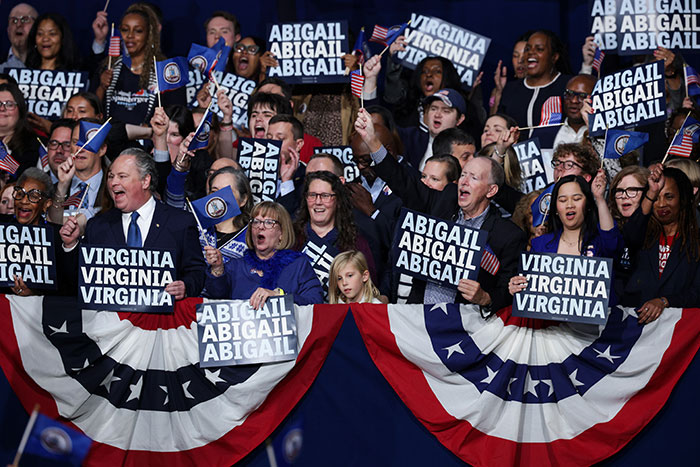 Supporters celebrate Virginia turning blue with signs for Abigail, waving flags at a political event amid Trump election challenges.