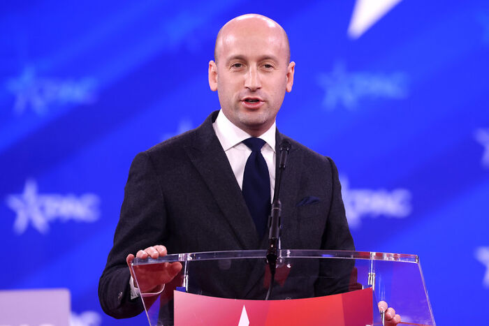 Man in suit speaking at a podium during a conference with a blue background featuring white star logos.