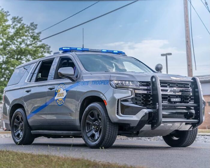 State trooper police SUV with blue lights on, parked on a street near a house fire scene involving children and family injuries.