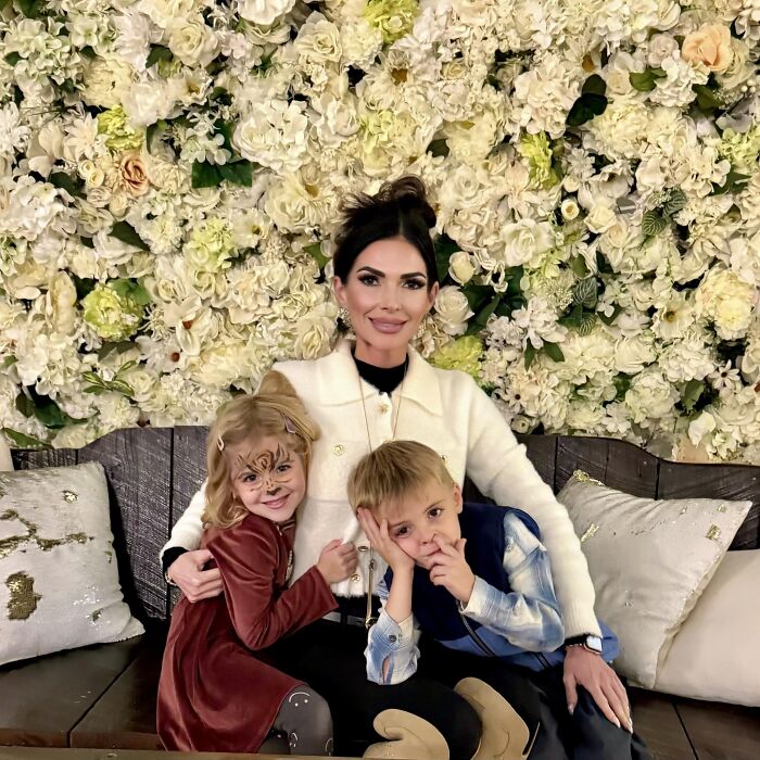 Mom with twin 6-year-olds sitting on a bench, surrounded by floral background, involved in mansion tragedy amid divorce.
