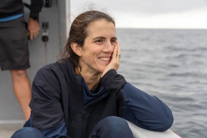 Woman with dark hair sitting and smiling on a boat, reflecting a calm moment amid news of Kennedy attacks.