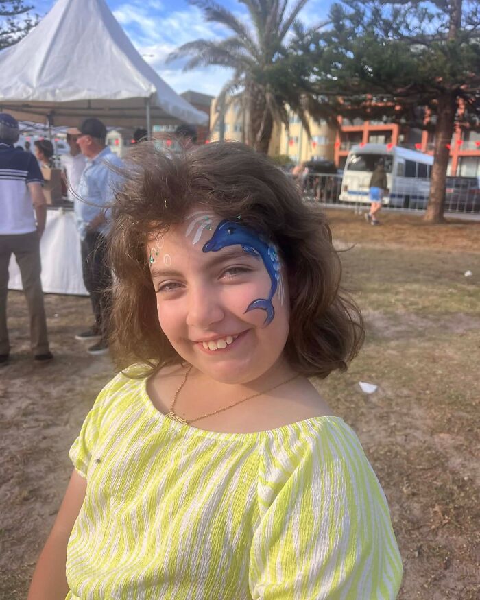 Smiling girl with dolphin face paint at an outdoor event near Bondi Beach on a sunny day.