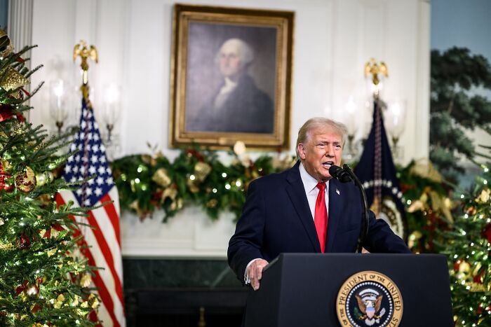 Former President Trump delivering a TV address with holiday decorations and American flags in the background.