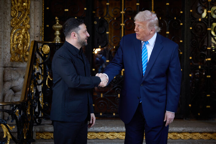 Volodymyr Zelenskyy and Donald Trump shaking hands outside a building, Zelenskyy&rsquo;s facial expression notable after Trump&rsquo;s Putin claim.