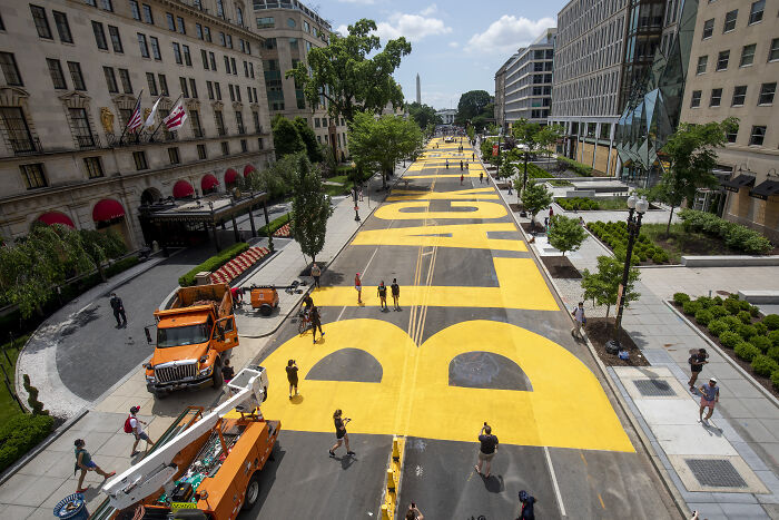 BLM Plaza in Washington DC with large yellow letters painted on the street and people walking along the area.