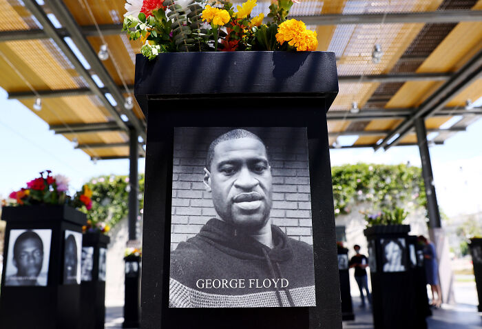 Black and white image of George Floyd displayed on a pedestal with flowers at BLM Plaza amid renaming debate involving Nancy Mace and Charlie Kirk.