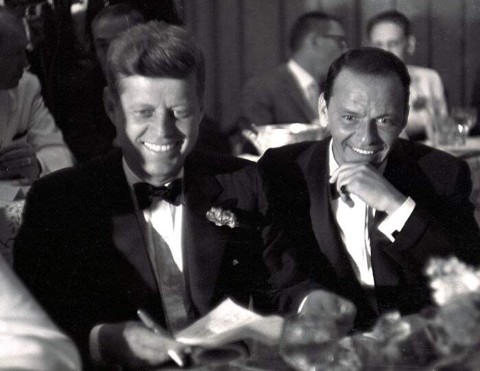 Black and white photo of John F. Kennedy and Frank Sinatra smiling at a formal event, related to Nancy Sinatra Trump supporter remarks.