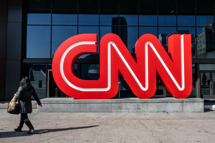 Person walking past large CNN logo outside building, illustrating CNN news and Kalshi partnership concept.