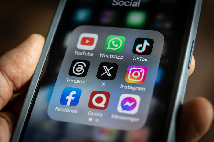 Smartphone screen showing social media apps including YouTube, WhatsApp, TikTok, X, and Instagram on a dark background.