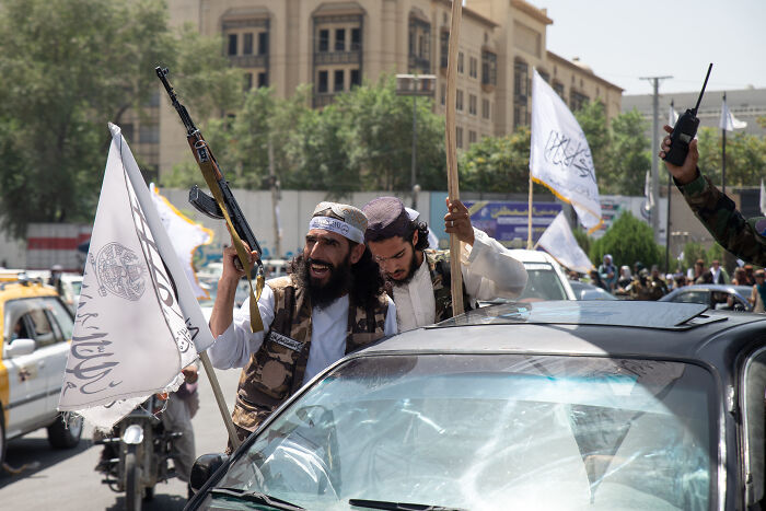 Taliban fighters holding rifles and flags during a street gathering in an urban area amid political tensions.