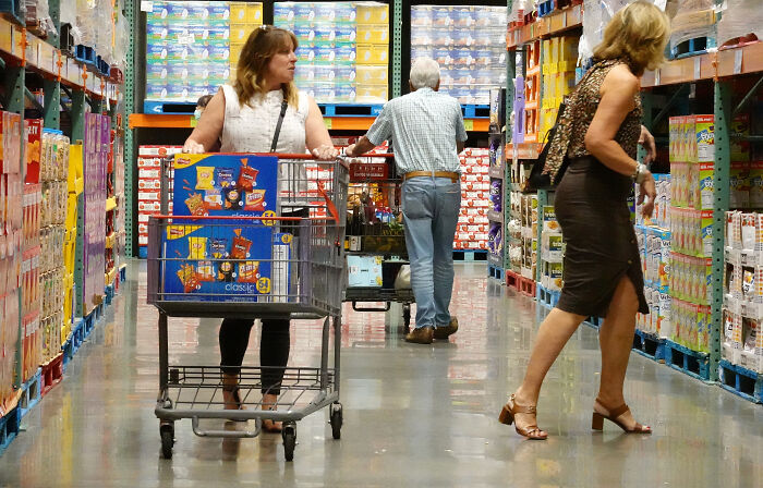 Shoppers with carts navigate aisles stocked with bulk goods in a Costco store amid tariff and court dispute news.
