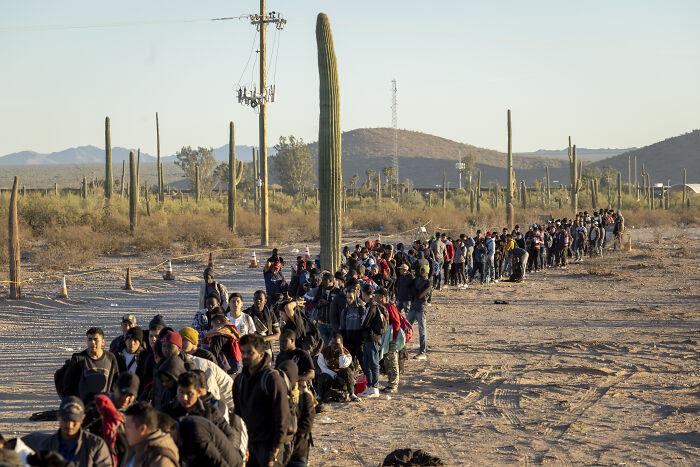 Large group of migrants walking in desert landscape under sunset, reflecting border and immigration issues linked to Trump claims.