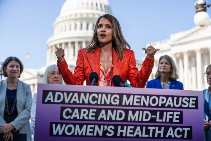 Halle Berry speaking at a podium about women&rsquo;s health care, with the US Capitol building visible in the background.